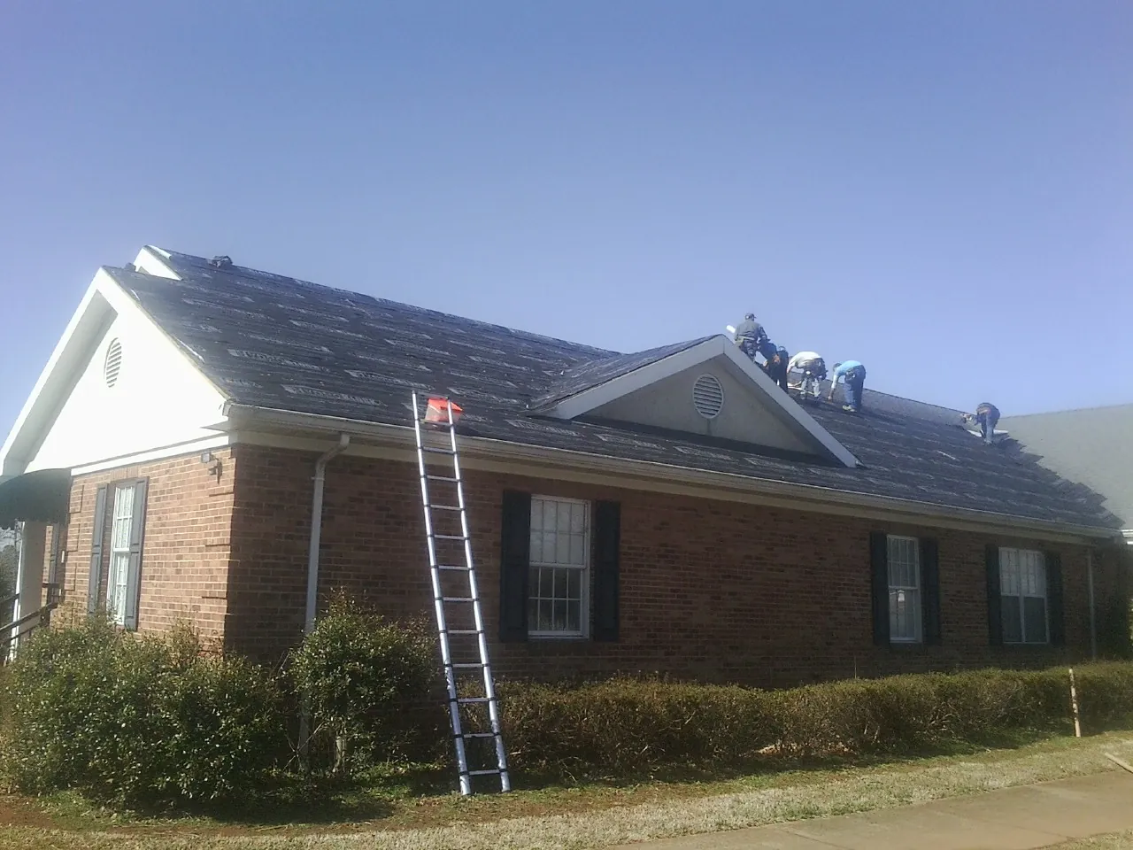 Crew tearing shingles off a brick ranch roof with a ladder set — Metal Roof Repair work by our crew in Dugway