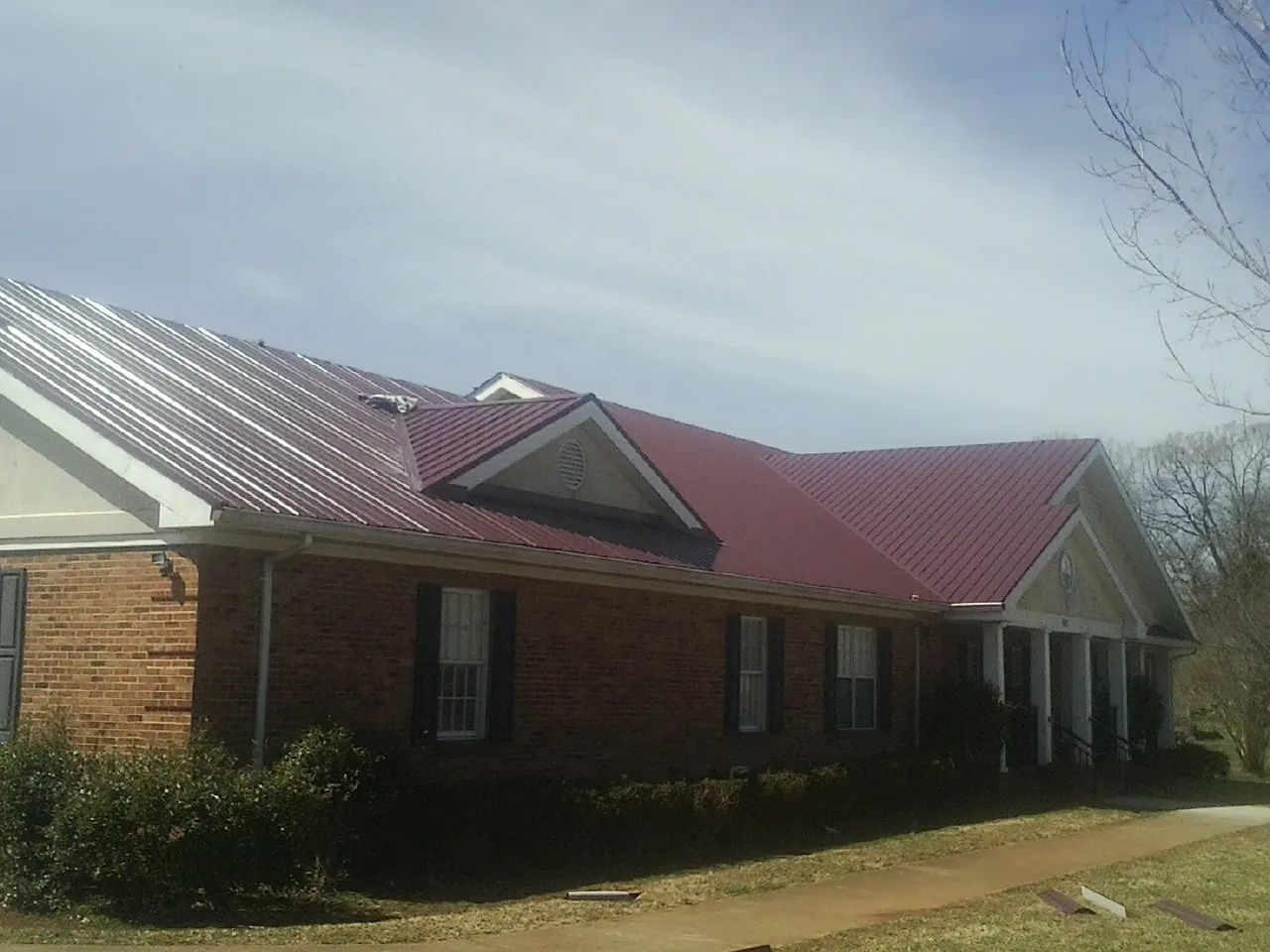 Red metal roof with gabled entries on a long brick building, from a Hail Damage Roof Repair job in Dugway