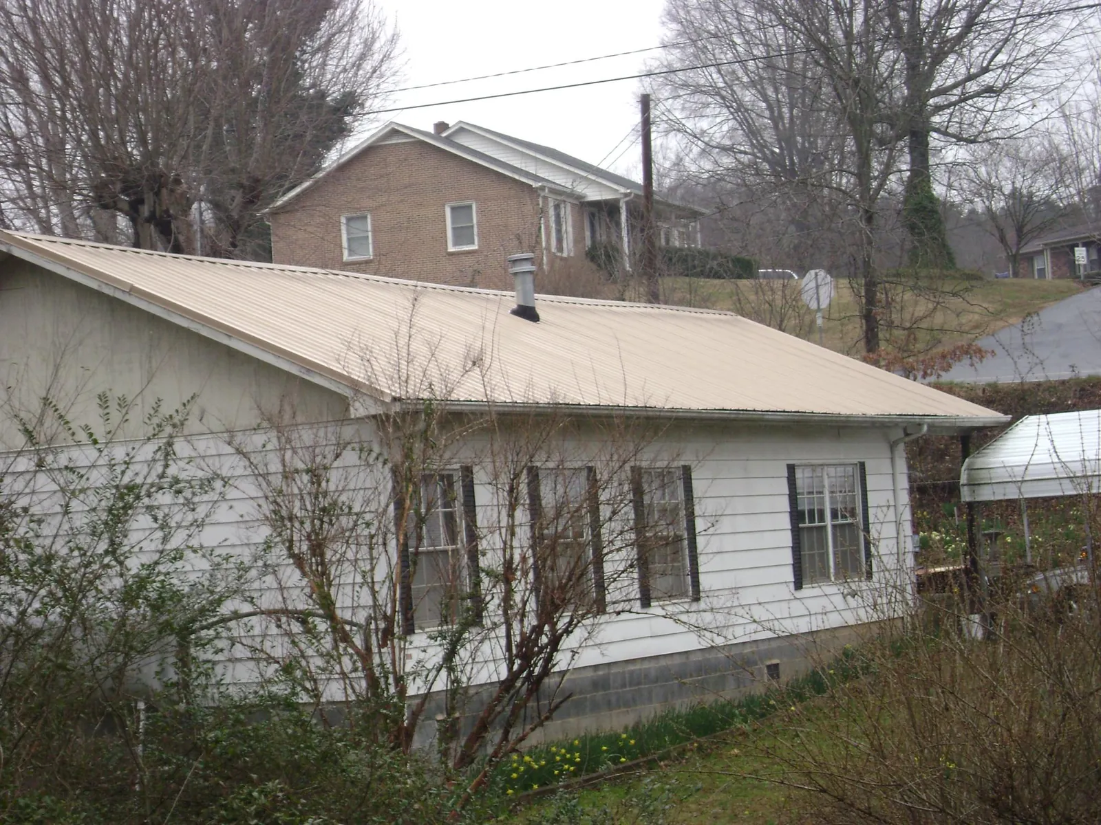 Tan metal roof on a white sided house set into a hillside — Commercial Roofing by Roofing Brothers in Dugway